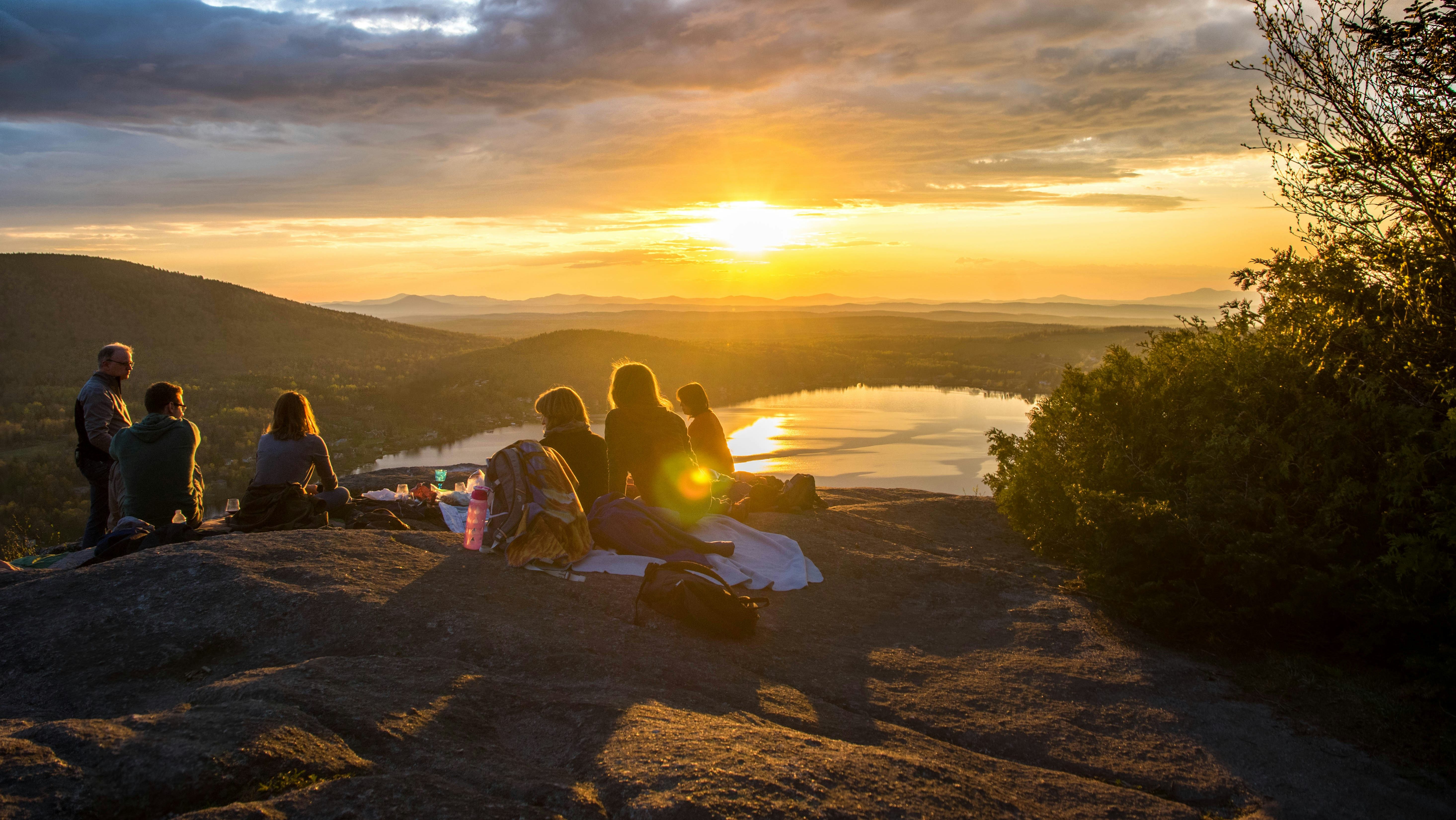 Grupo de personas arriba de una montaña conviviendo y al fondo la escena del ocaso